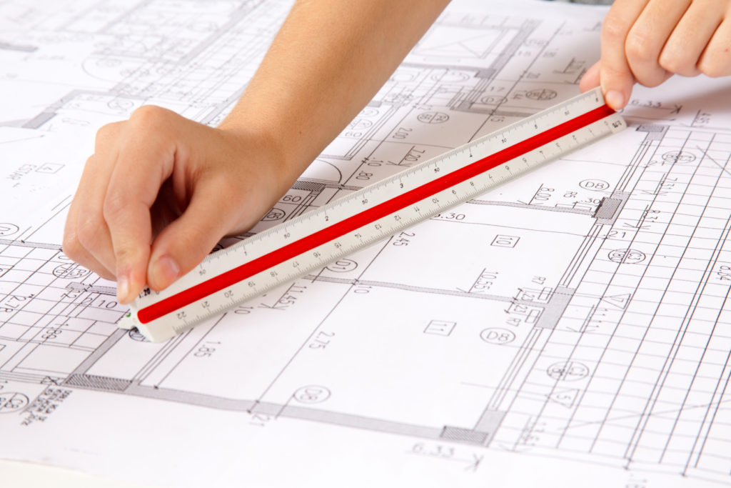 Two hands using a scale ruler on a set of blueprints